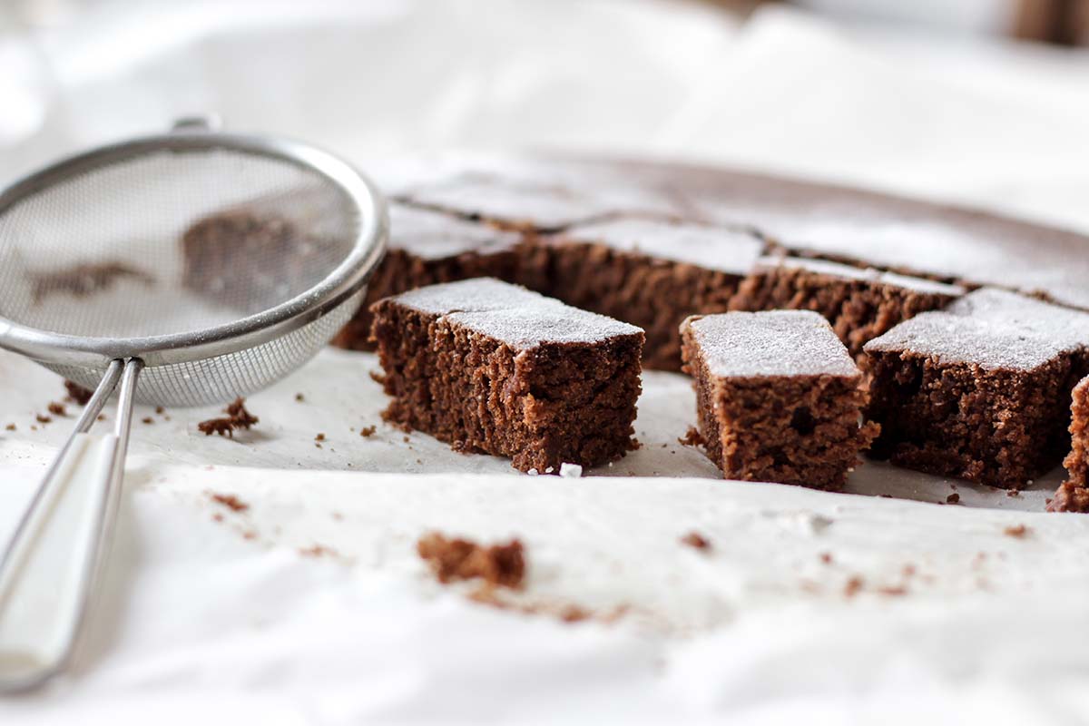 Brownies on parchment paper next to a sifter