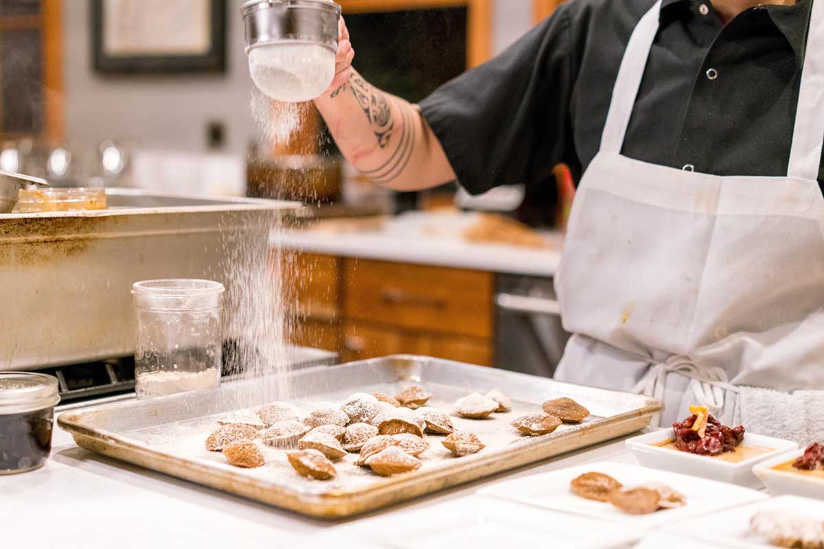 Chef sprinkling powdered sugar on madeleines