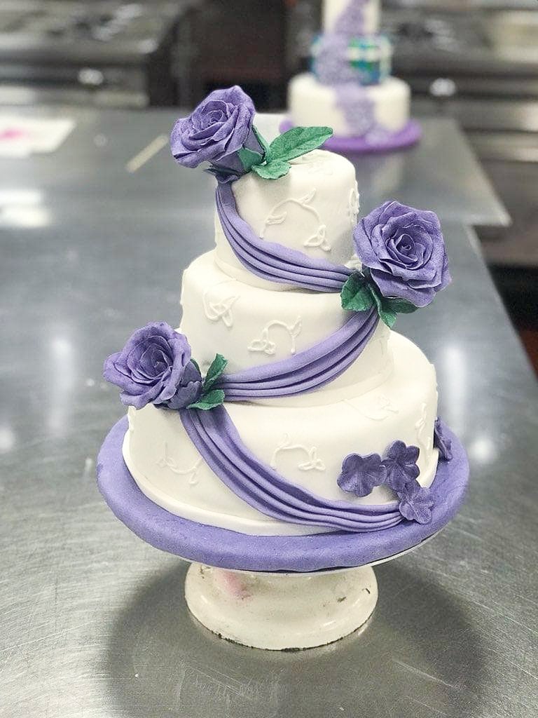 Three-tiered white wedding cake with purple roses and purple sash