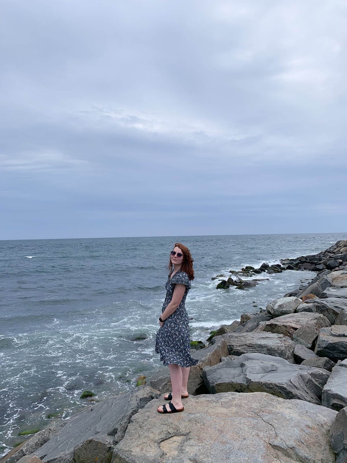 Girl standing on top of rocks next to crashing ocean waves