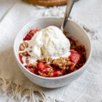 Bowl of strawberry cardamom crisp topped with ice cream and a spoon