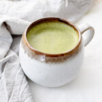 Mug of oat milk matcha latte in front of a grey napkin