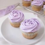 Two Earl Grey and lavender cupcakes on a plate with a piping bag behind them