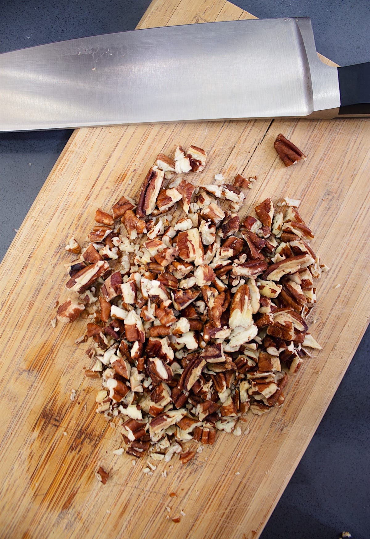 Chopped pecans resting on a cutting board next to a knife