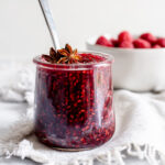 Jar of raspberry jam in front of a bowl of raspberries