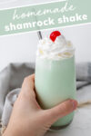 Hand holding shamrock shake topped with cherry and text that reads 'Homemade Shamrock Shake'