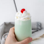 Hand holding a glass of shamrock shake topped with a cherry