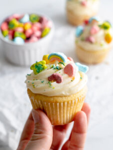 Hand holding a cupcake topped with frosting and Lucky Charms