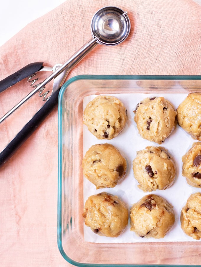 Overhead shot of cookie dough balls and a cookie scoop on a pink napkin