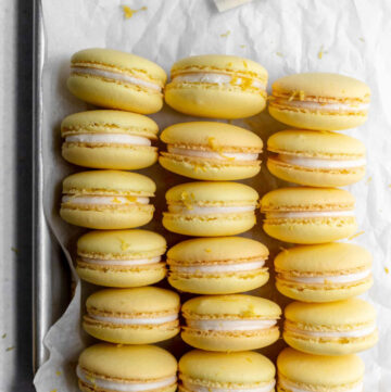 Lemon macarons sitting on a baking sheet next to piping bags with buttercream and lemon curd