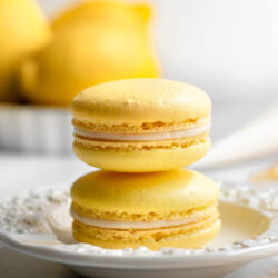 Two lemon macarons stacked on a white plate with text that reads 'Homemade Lemon Macarons'