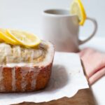 Earl grey and lemon loaf cake with lemons sitting on top with mug of tea behind it
