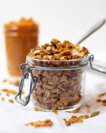 A canister of pumpkin granola with a jar of pumpkin in the background