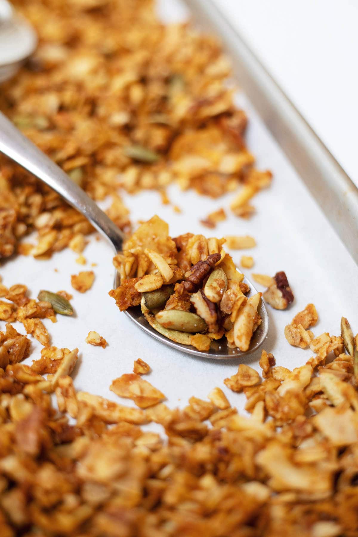 A spoonful of pumpkin granola on top of a tray of granola