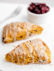 Two pumpkin cranberry scones in front of a bowl of dried cranberries