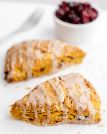 Two pumpkin cranberry scones in front of a bowl of dried cranberries
