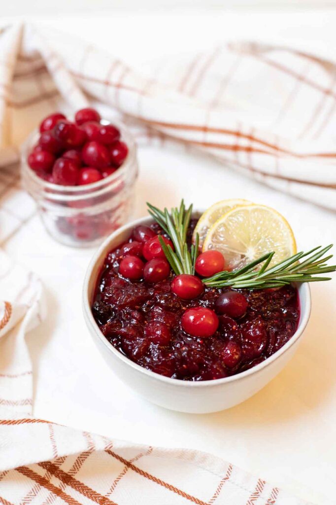 Bowl of cranberry sauce topped with rosemary and lemons