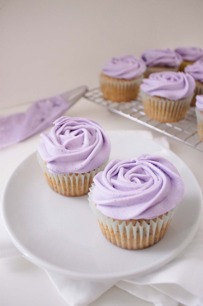 Two earl grey and lavender cupcakes on a plate with several others behind them