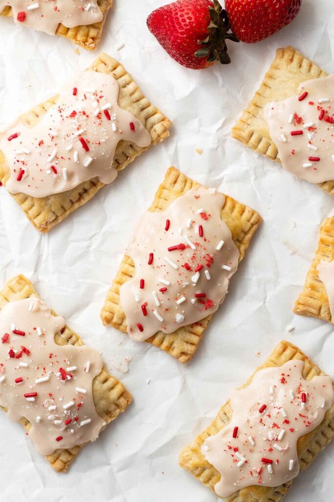 Strawberry pop tarts on top of parchment with strawberries next to them