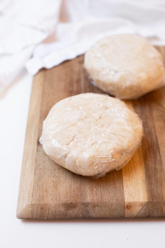 Two disks of pie dough wrapped in parchment on a cutting board