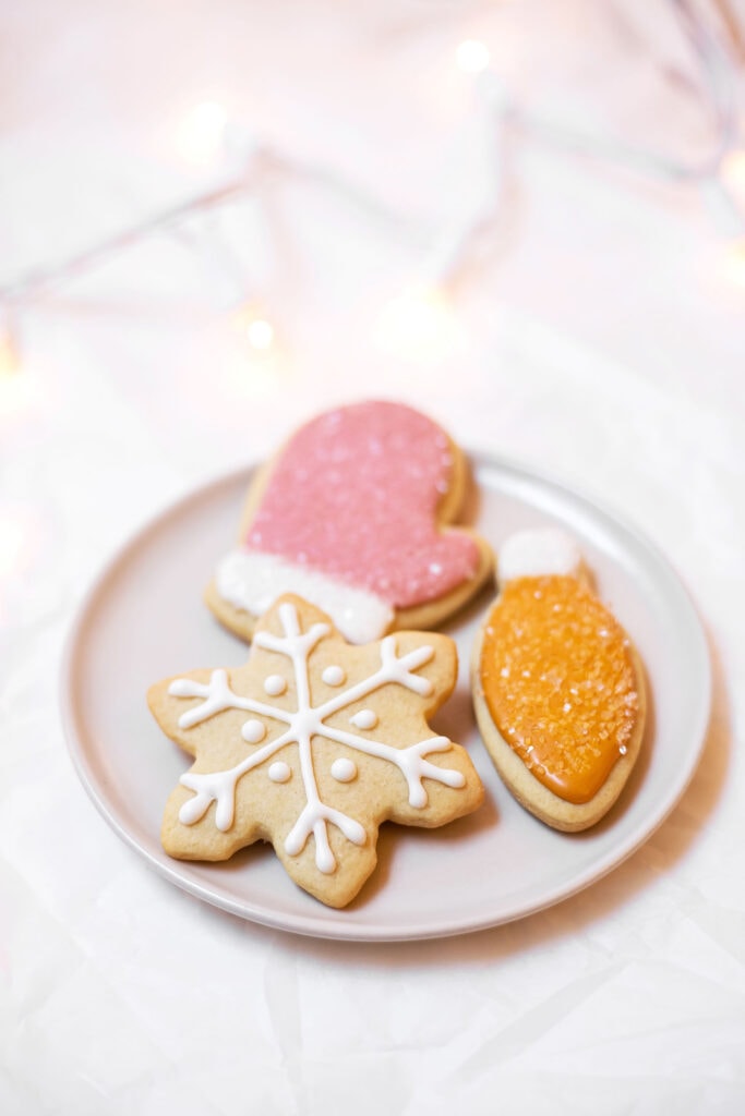 A plate filled with three Christmas cookies: a pink mitten, an orange light, and a white snowflake