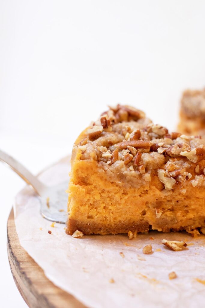 Spatula lifting up sweet potato casserole cheesecake from a cake stand