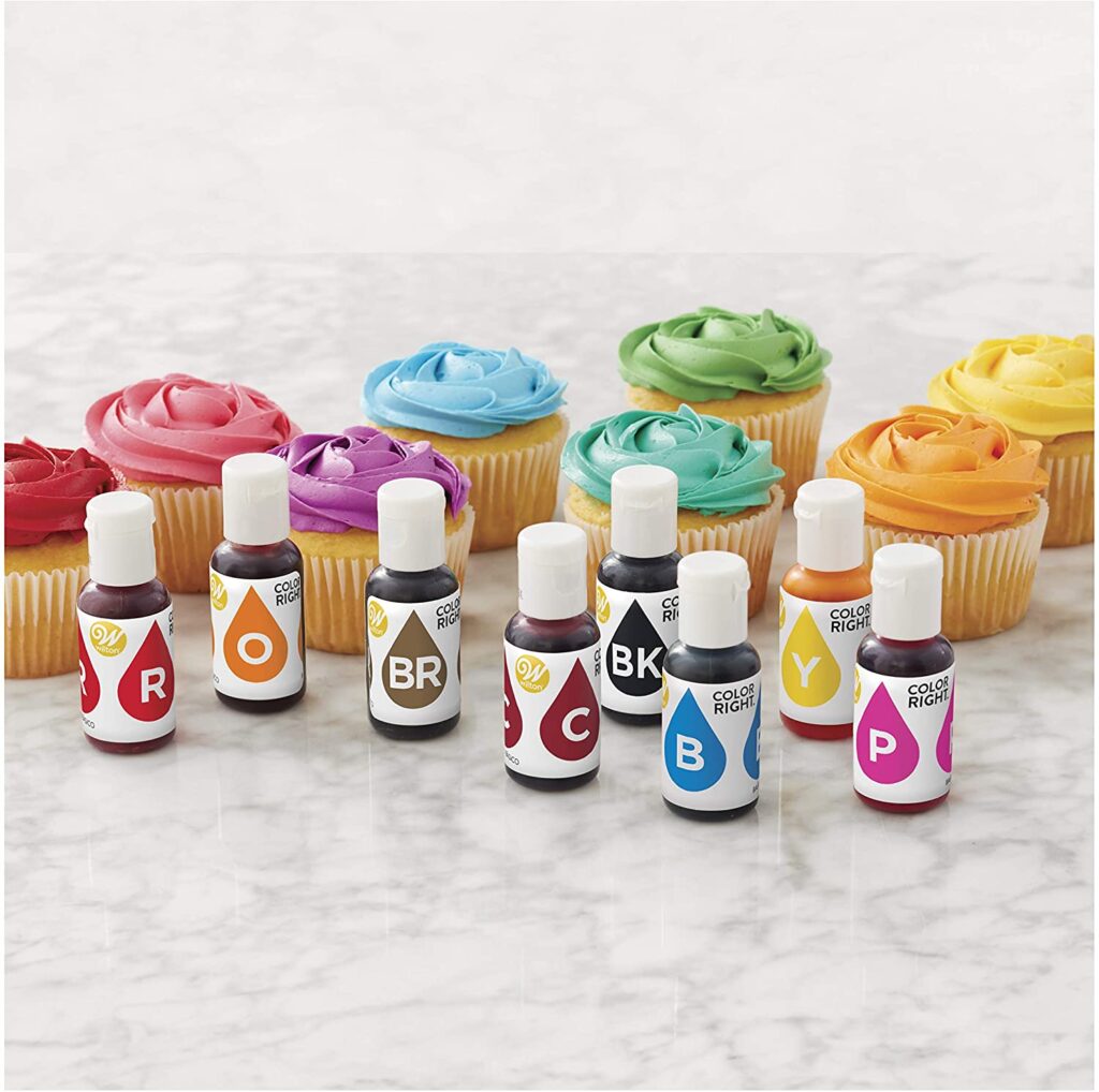 Wilton food coloring set in front of different colored cupcakes