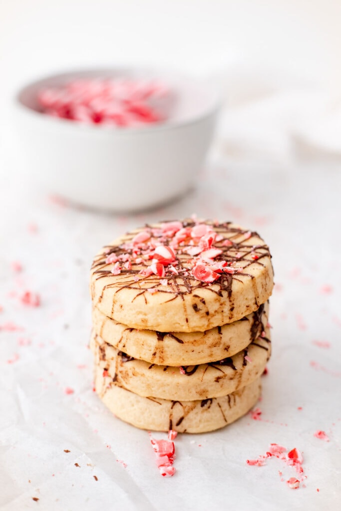 A stack of chocolate peppermint shortbread cookies in front of a bowl of candy canes