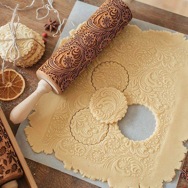 Engraved rolling pin next to cookie dough that has been cut out