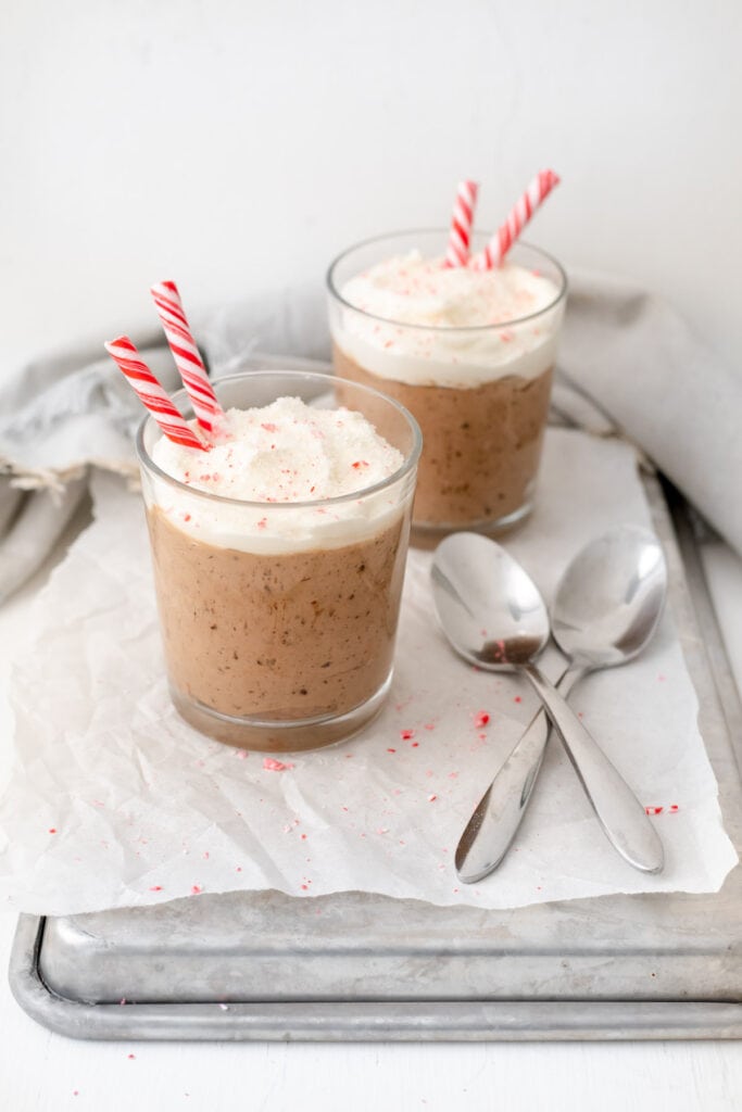 Two glasses of mousse topped with fresh whipped cream and candy canes