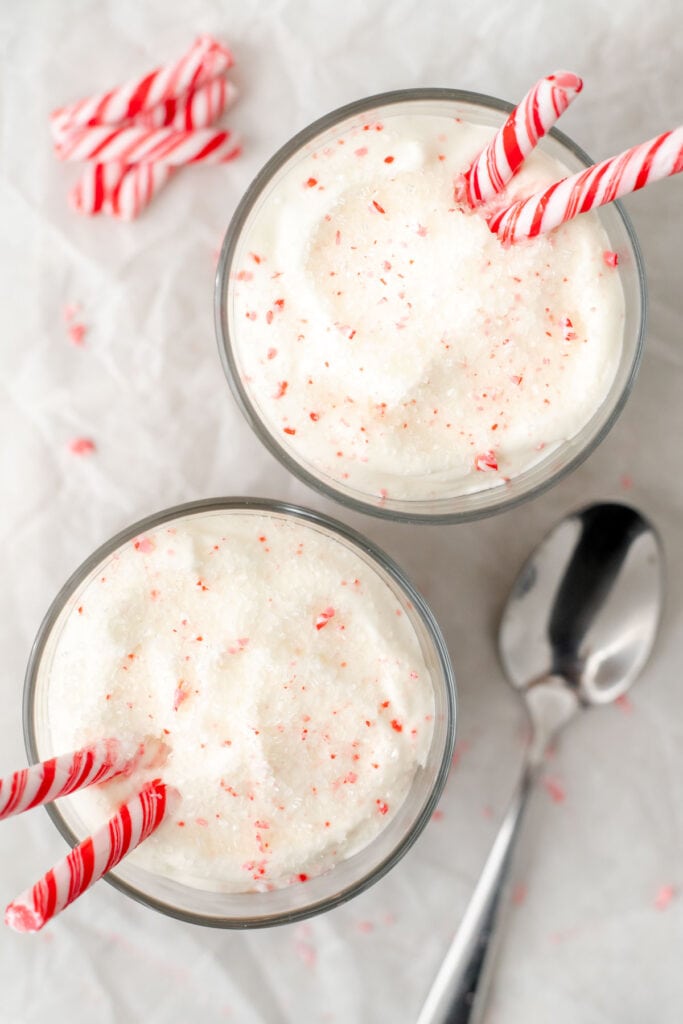 Two glasses of mousse topped with whipped cream and candy canes viewed from above