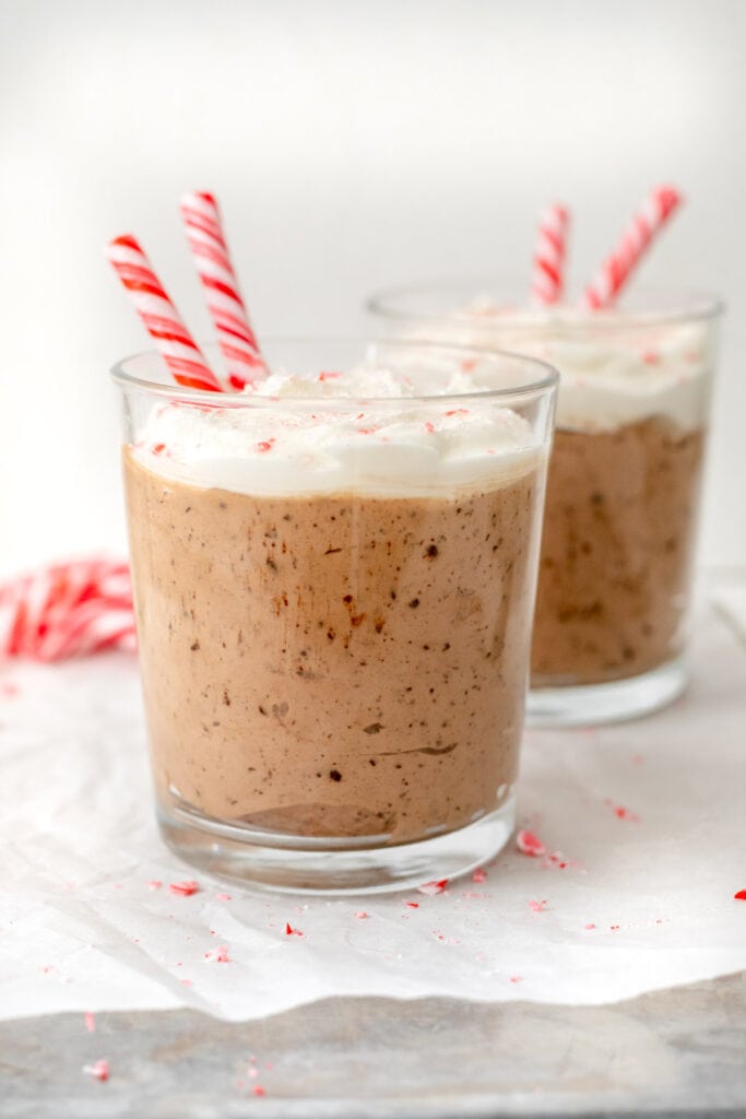 Two glasses of chocolate mousse topped with whipped cream and candy canes 