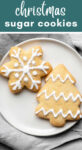 Two sugar cookies resting on a plate on top of a grey napkin with text that reads 'Christmas sugar cookies'