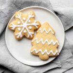 Two sugar cookies resting on a plate on top of a grey napkin