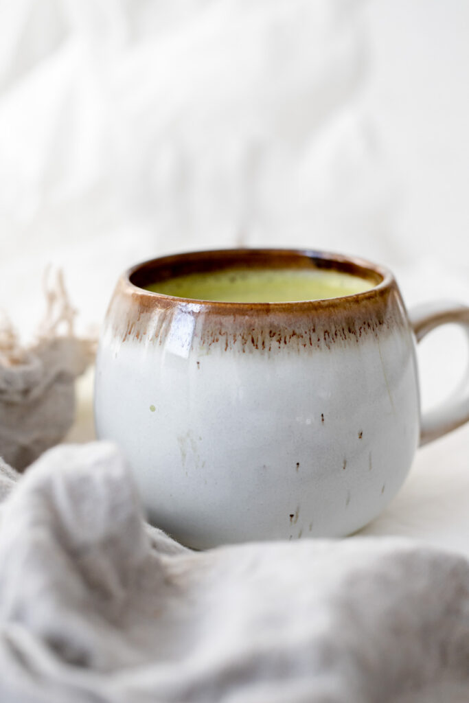 A mug of oat milk matcha latte next to a grey napkin 