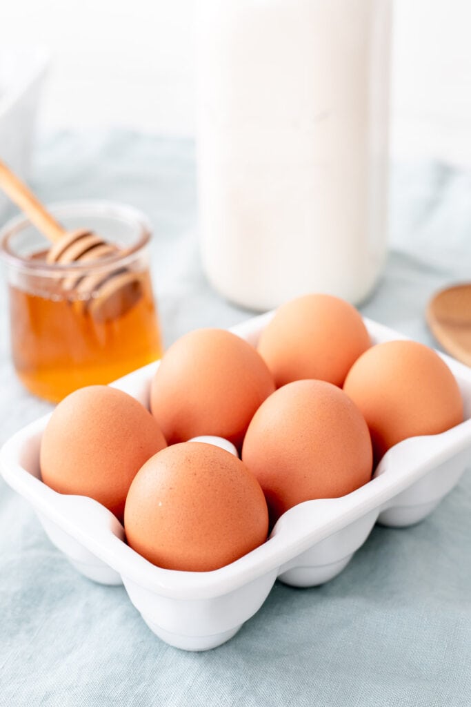 Carton of eggs, a pot of honey, a milk jug, and a wooden spoon