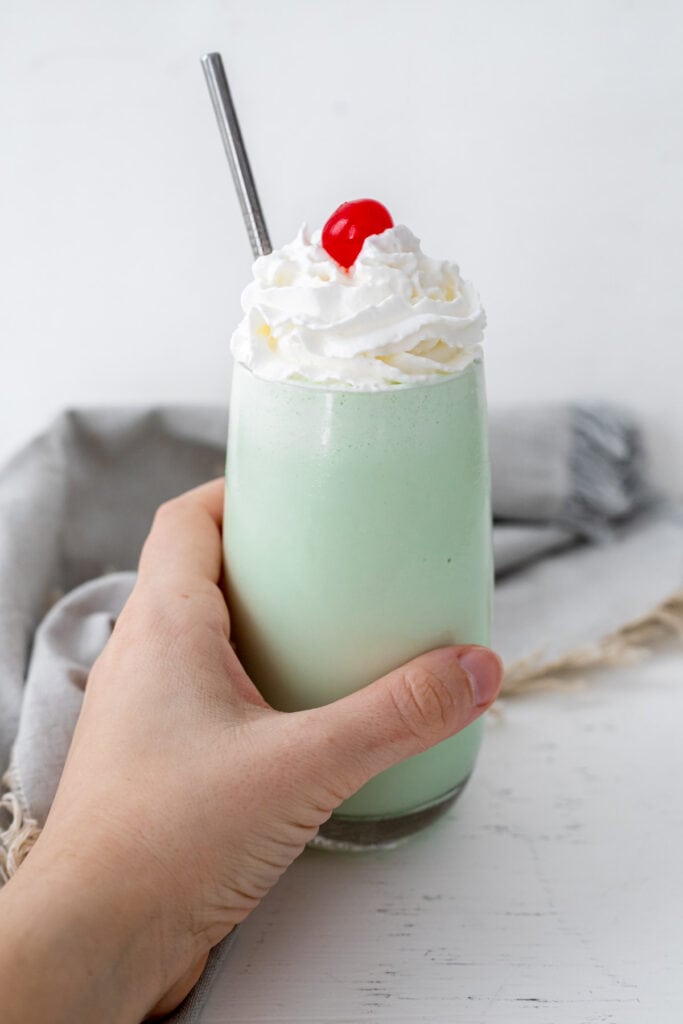 Hand holding a glass of shamrock shake topped with a cherry