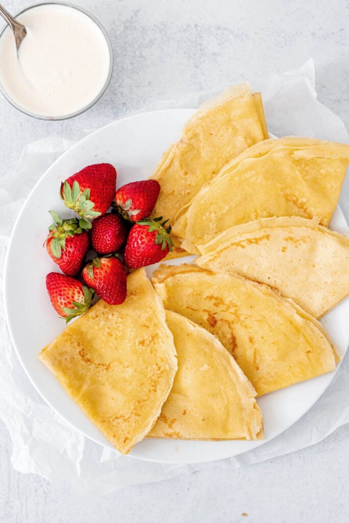 Overhead shot of crepes on a plate with strawberries and a bowl of whipped ricotta