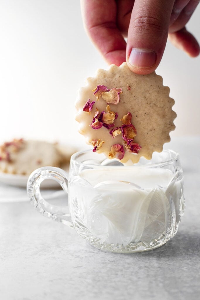 Hand dunking rose cardamom shortbread cookie into a cup of milk