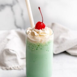 Shamrock shake in a glass topped with whipped cream and a maraschino cherry