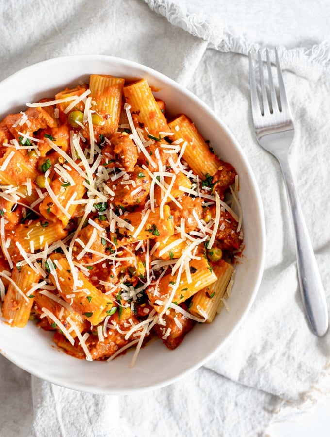 Overhead shot of rigatoni with sausage and peas in a bowl next to a fork