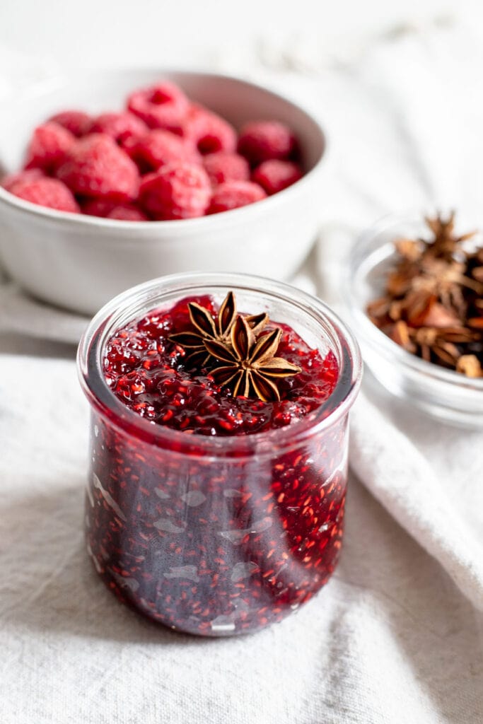 Jar of raspberry jam with a few pieces of star anise resting on top