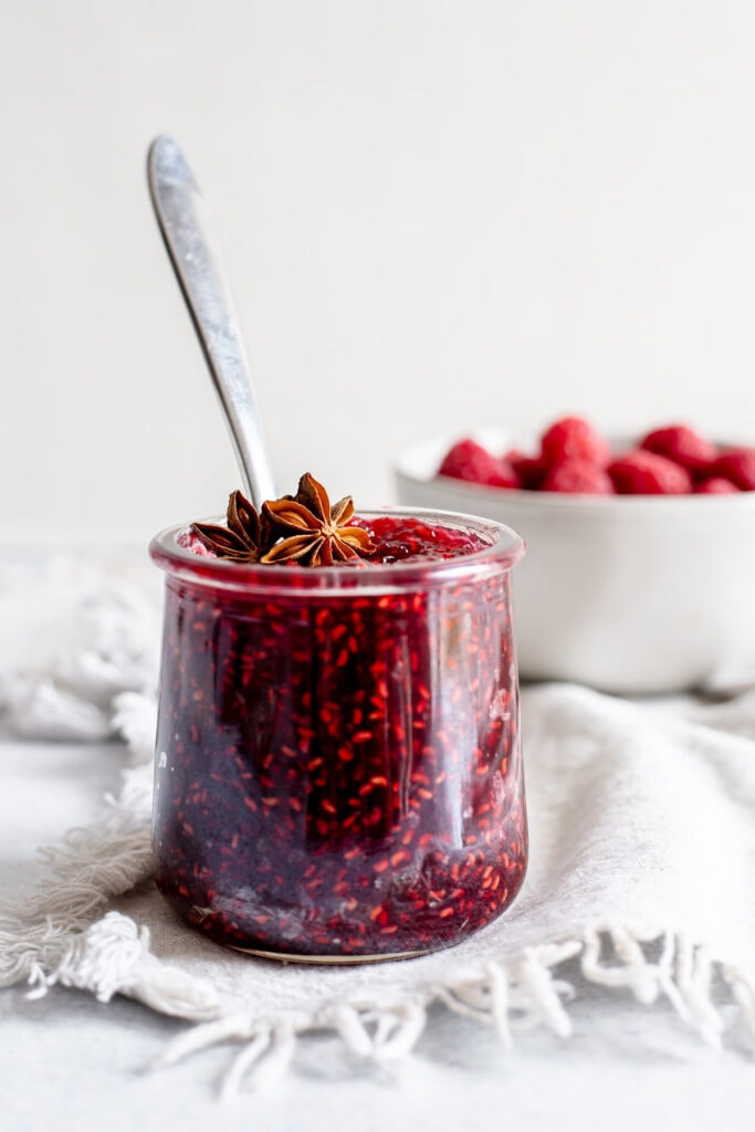 Jar of raspberry jam in front of a bowl of raspberries