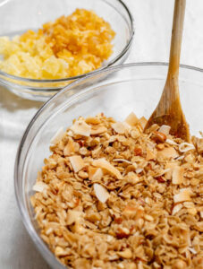 Bowl of granola with spoon next to a bowl of drried mango and dried pineapple