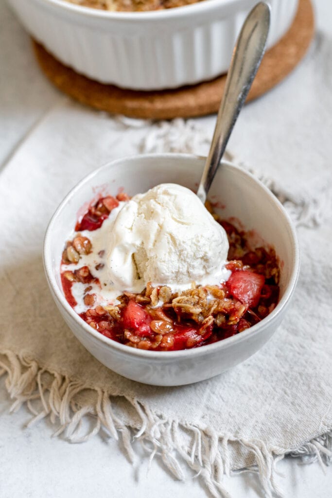 Bowl of strawberry cardamom crisp with ice cream on top and spoon resting in it