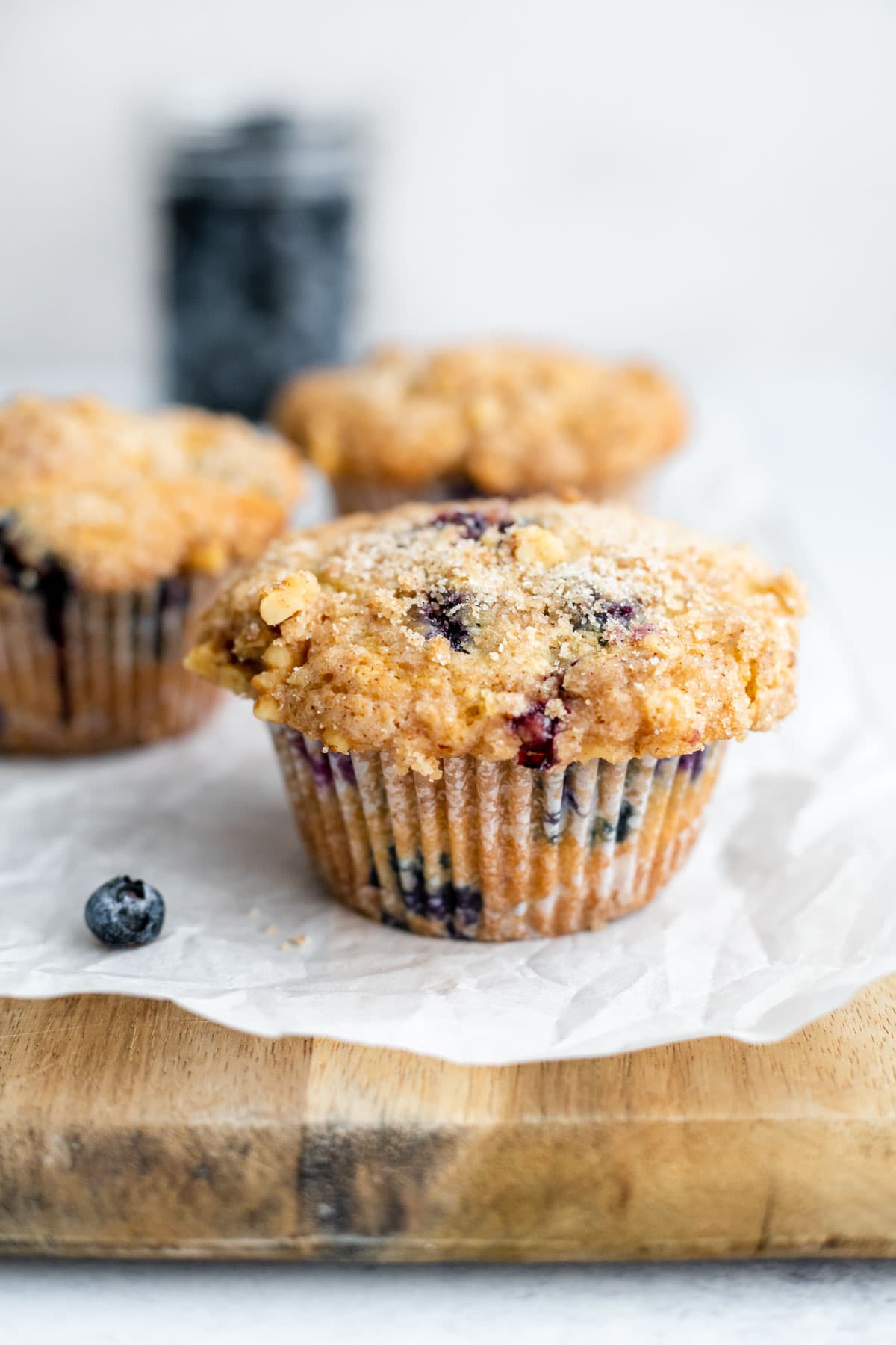 Three blueberry muffins resting on a cutting board in front of a jar of blueberries