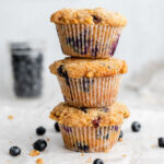 Stack of three blueberry muffins in front of a bowl of blueberries