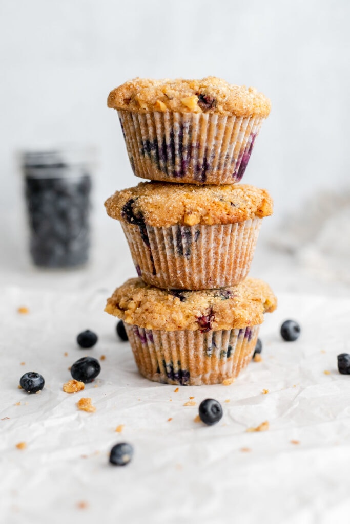 Three blueberry muffins stacked on top of each other in front of a jar of blueberries