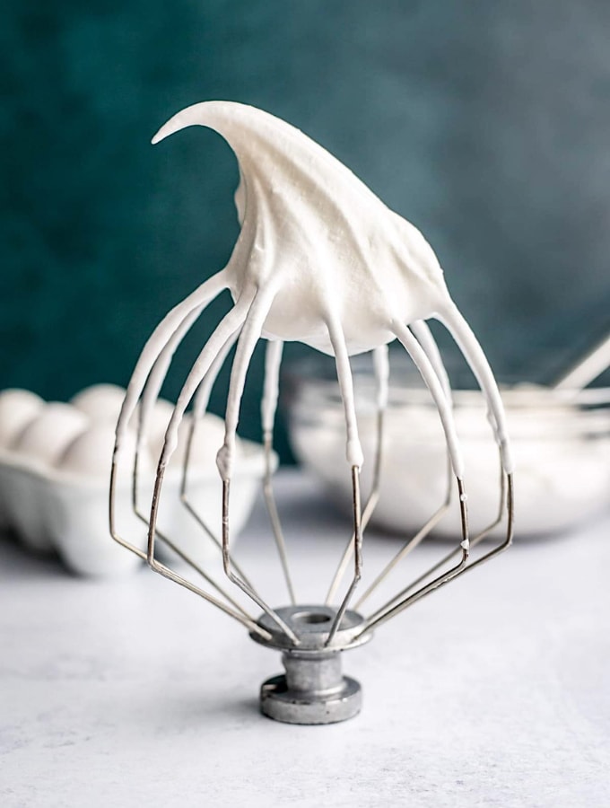 Whisk attachment with Italian meringue in front of eggs and a bowl of meringue