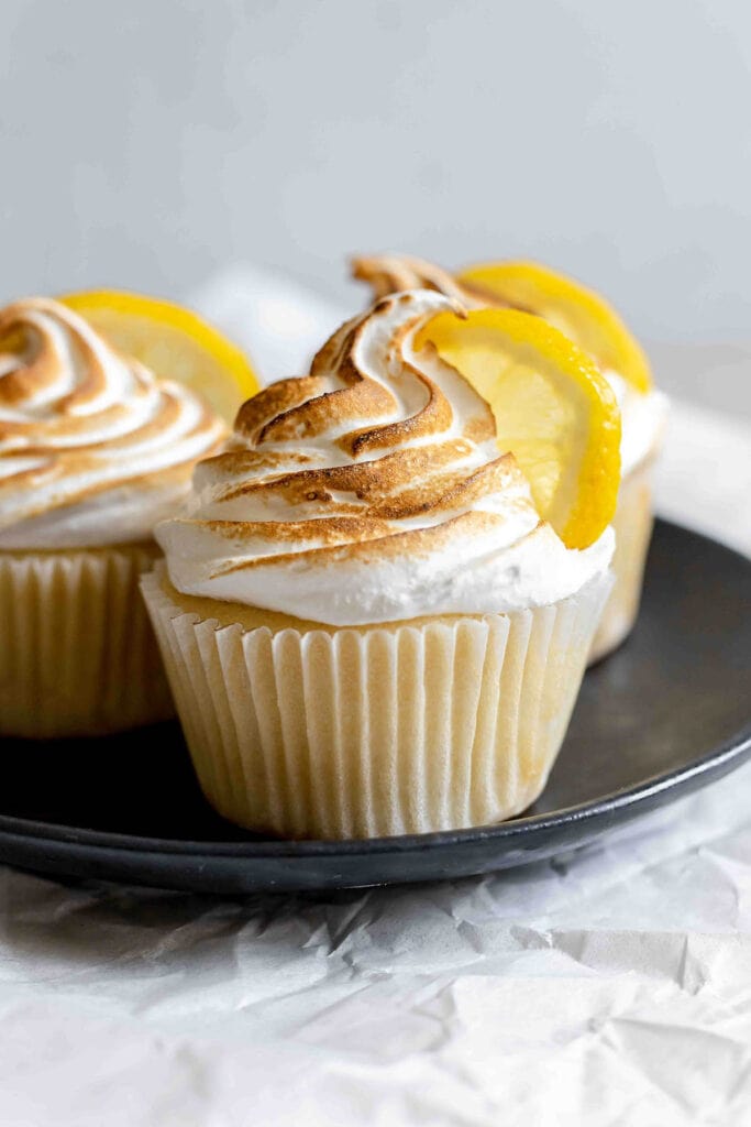 Three lemon meringue cupcakes on top of a black plate